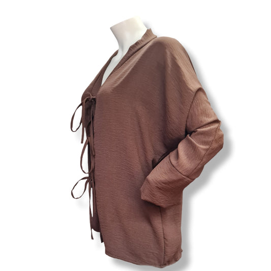 Perfekt, danke für die Stoffangabe! Hier ist die überarbeitete und detaillierte Produktbeschreibung:
---
## 🌸 Produktbeschreibung: Bluse mit Bindedetails – Eleganz trifft Komfort
### ✨ Design
Diese stilvolle Langarmbluse in warmem Braunton ist ein echter Hingucker für jede Garderobe. Der tiefe V-Ausschnitt wird durch drei dekorative Bindeschleifen entlang der Vorderseite betont – ein verspieltes Detail, das gleichzeitig für eine individuelle Passform sorgt. Die lockeren Ärmel mit leicht zulaufenden Mans