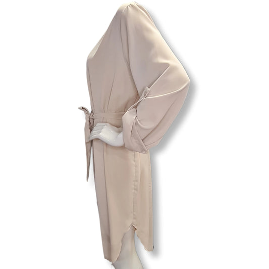 Tunikakleid in Sandfarben mit Gürtel geknotet und V-Ausschnitt.Die Ärmel sind gekrempelt und mit Spange aus Stoffe befestigt.