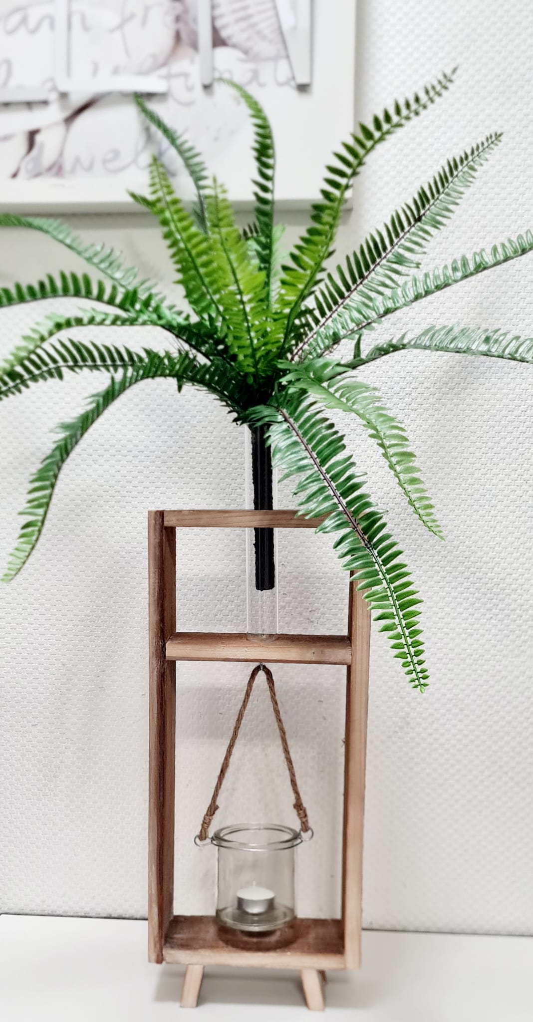 Diese Regalvase aus Akazienholz bietet eine einzigartige Möglichkeit, Trocken- oder echte Blumen in einem Reagenzglas aufzustellen. Das hängende Glas mit Kokos Kordel kann auch für Kerzen oder Teelichter genutzt werden. Ein vielseitiges und dekoratives Element, das sowohl natürliche als auch künstlerische Elemente in Ihr Zuhause bringt. Dekoriert mit Farn und Teelicht.