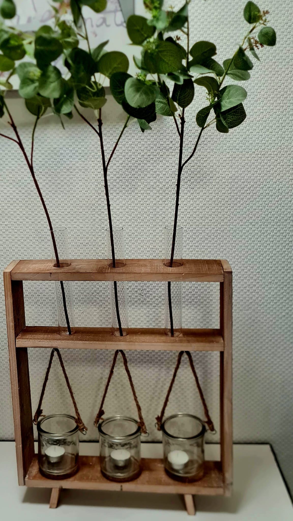 Diese einzigartige Regalvase aus Akazienholz ist mit 3 Reagenzgläsern und 3 Gläsern, die mit Kokos Kordel befestigt sind, perfekt für Kerzen oder Teelichter. Schaffen Sie eine gemütliche Atmosphäre und setzen Sie Akzente in Ihrem Zuhause. Ein stilvolles und funktionales Wohnaccessoire für jeden Anlass. Dekoriert Vorderansicht mit 3 Gräser und 3 Teelichtkerzen